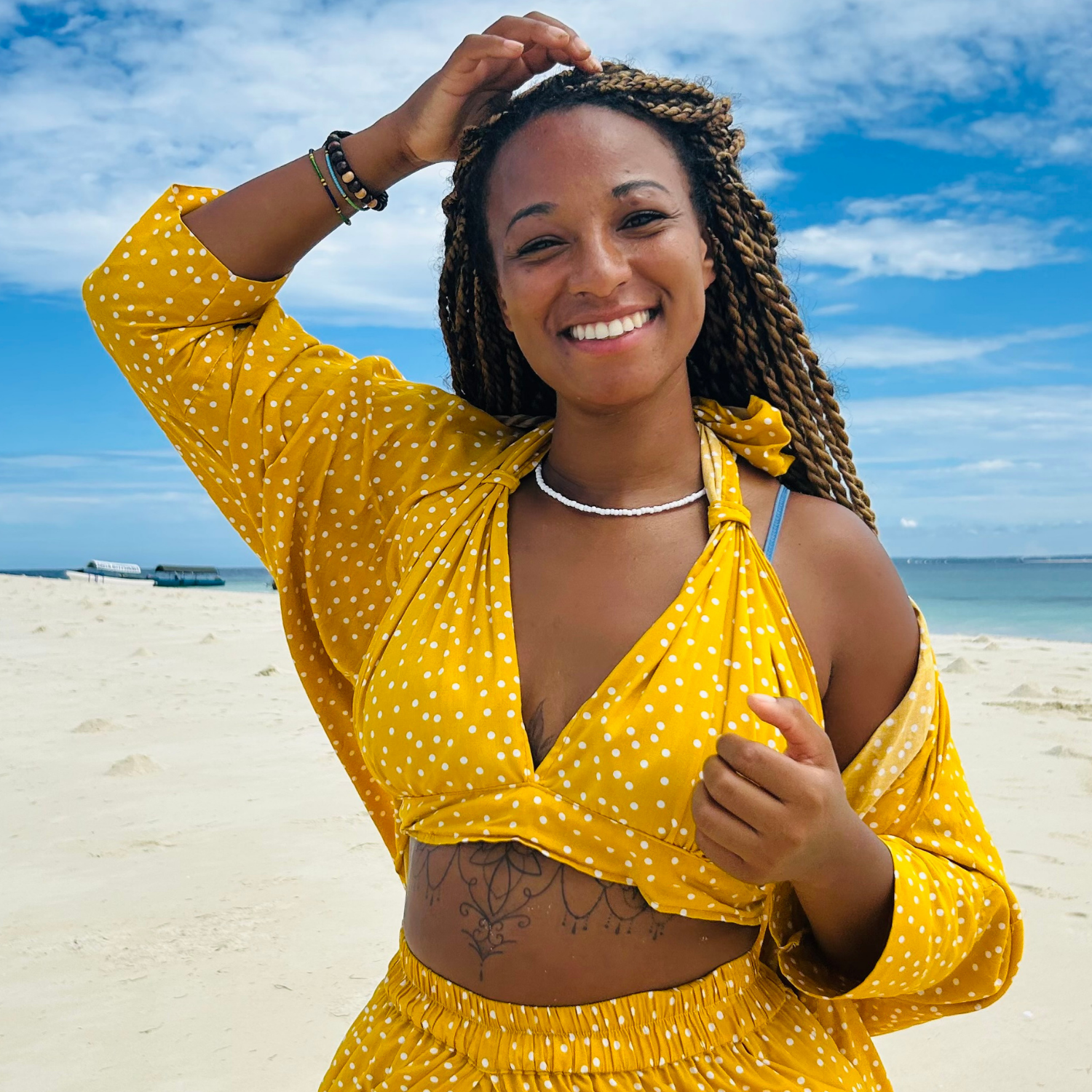 Lakisha, founder of Goldenweeks, smiling on a white sand Zanzibar beach in yellow outfit