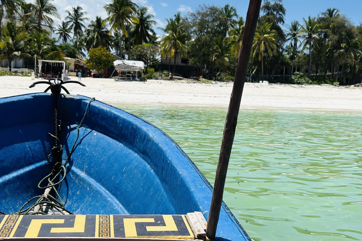 Traditional wooden dhow boat on clear turquoise water near a white Zanzibar beach